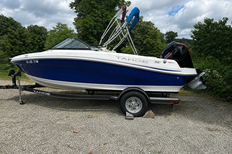 Slide: The Image of 2021 Tahoe 450 TS boat on trailer, parked on gravel, surrounded by greenery. - 1