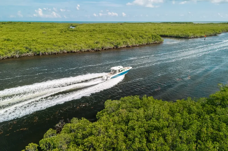 Slide: The Image of 2024 Boston Whaler 320 Vantage cruising through scenic waterway surrounded by lush greenery. - 19