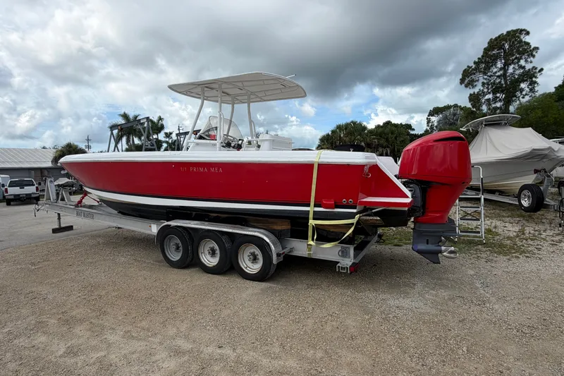 The Image of Red 2000 Intrepid 322 boat on trailer, parked outdoors under cloudy sky. - 1