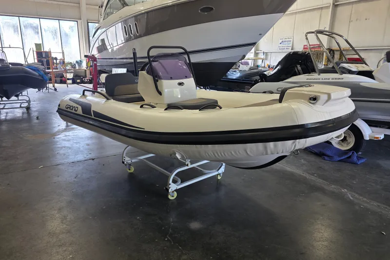 The Image of 2027 Grand Inflatables G380N boat displayed indoors on a wheeled stand. - 1