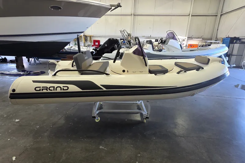 Slide: The Image of 2027 Grand Inflatables G380N boat in a showroom, featuring sleek design and modern seating. - 2