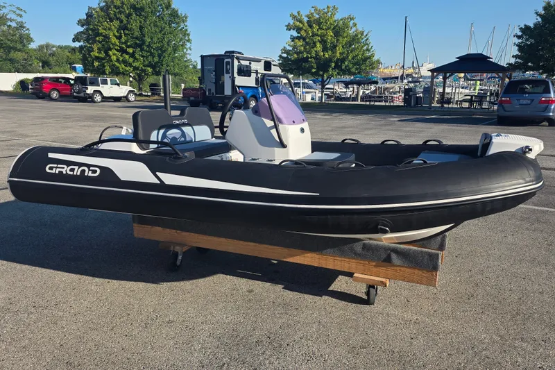 The Image of 2027 Grand Inflatables G380N boat displayed on a trailer in a marina parking lot. - 1