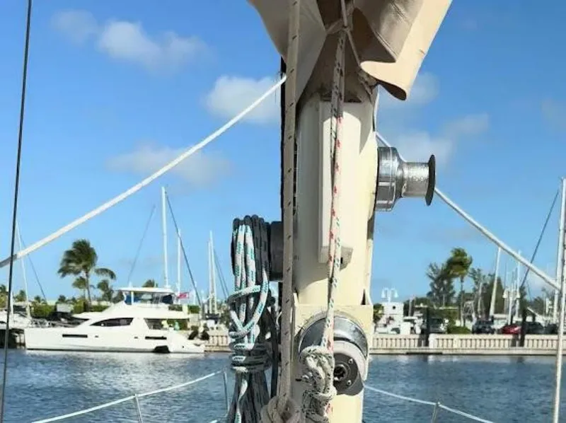Slide: The Image of A sailboat mast with ropes and pulleys, with a harbor and other boats in the background. - 5