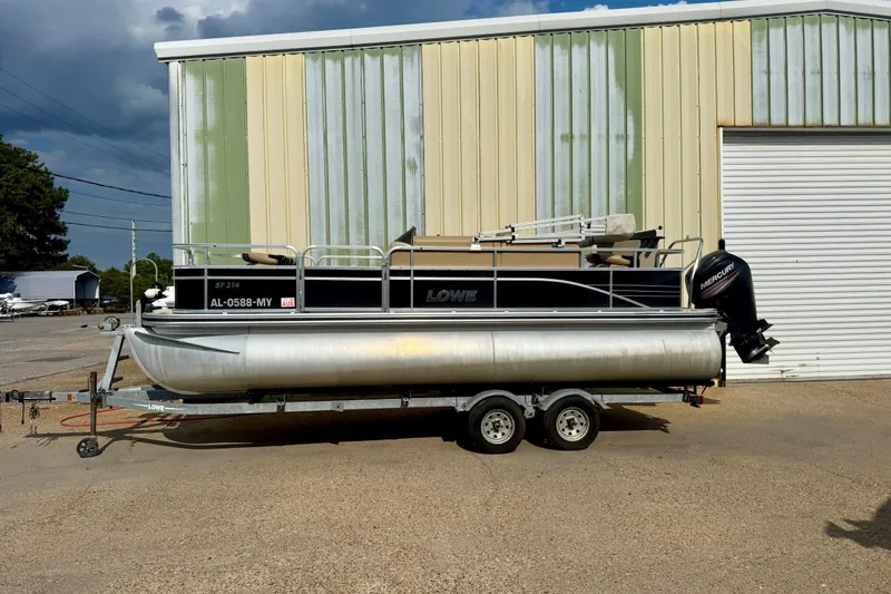 The Image of 2017 Lowe SF 214 Sport Fish pontoon boat on trailer, parked outside a warehouse. - 0