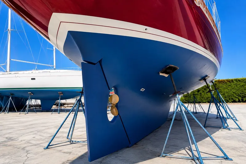 Slide: The Image of 1989 Mason 54 sailboat on stands, showcasing blue hull and red top under clear sky. - 6