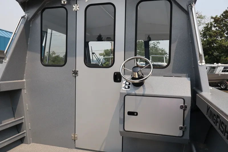 Slide: The Image of 2026 KingFisher 2225 Escape HT boat helm with steering wheel and cabin door. - 19