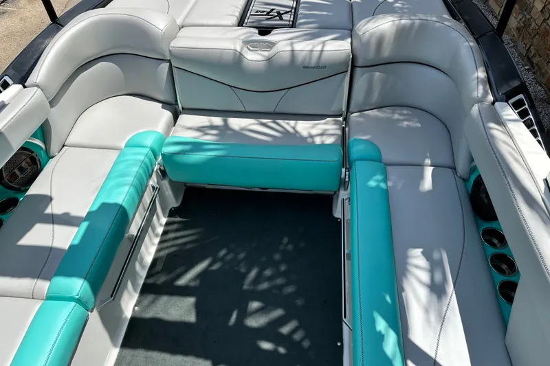 Slide: The Image of 2018 MasterCraft XT23 boat interior with white and teal seating, cup holders, and speakers. - 25
