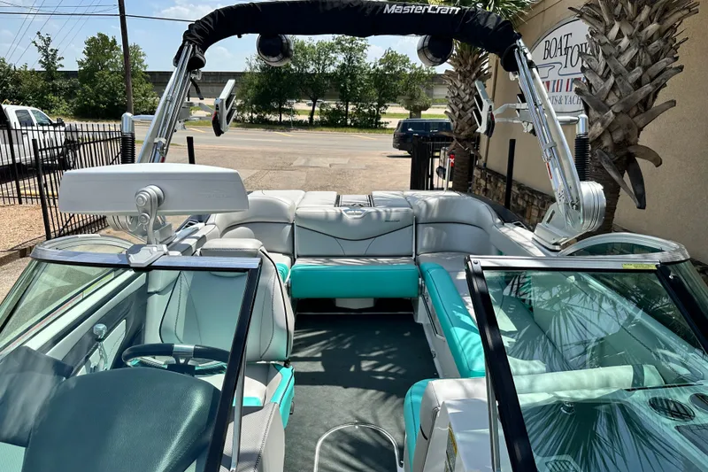 Slide: The Image of 2018 MasterCraft XT23 boat with teal and white interior, parked outdoors. - 31