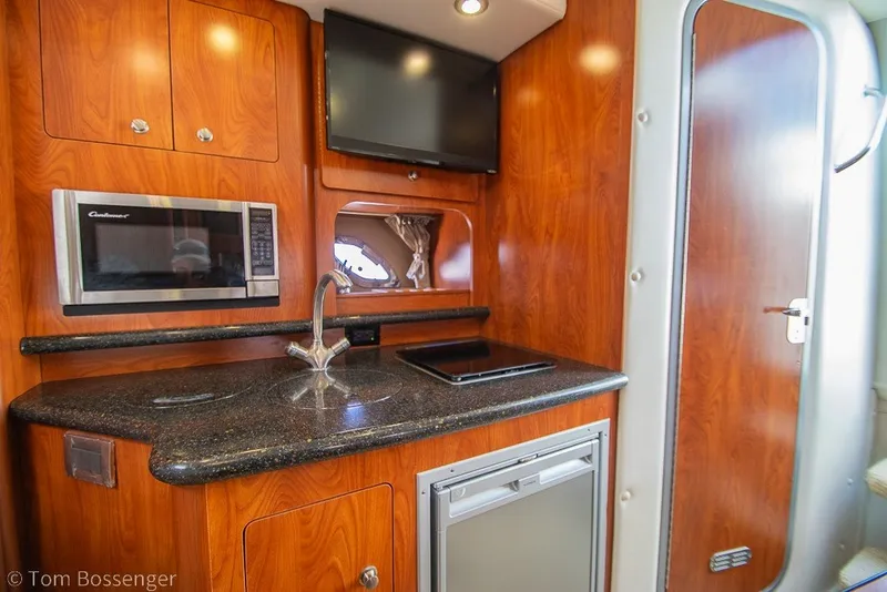 Slide: The Image of 2012 Rinker 310 Express Cruiser interior kitchen with microwave, sink, and wooden cabinetry. - 20