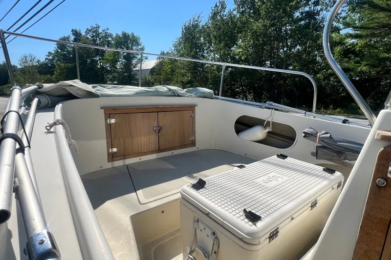 Slide: The Image of 1973 Boston Whaler 19 OUTRAGE boat interior with storage and cooler, surrounded by trees. - 21