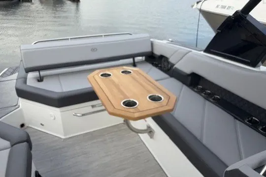 Slide: The Image of 2024 Cobalt R8 boat interior with gray seating and wooden table on a calm lake. - 10