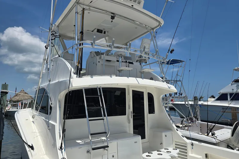 Slide: The Image of 2005 Cavileer 44 Convertible yacht docked, showcasing its spacious deck and flybridge under a clear sky. - 6