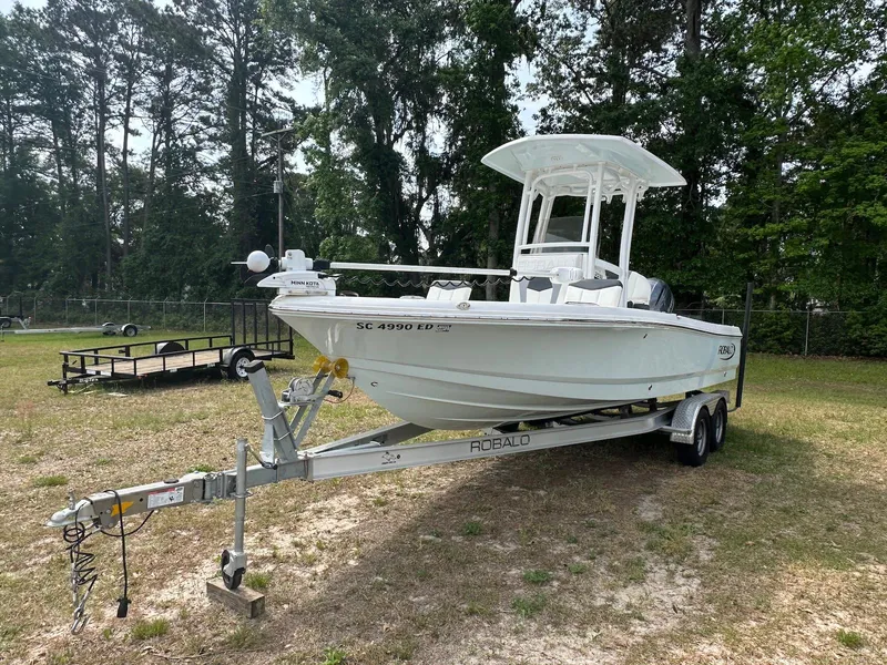 Slide: The Image of 2023 Robalo 226 Cayman boat on trailer, parked outdoors, surrounded by trees. - 1