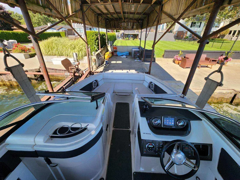 Slide: The Image of The image shows the cockpit of a 2015 Sea Ray 220 Sundeck boat docked under a covered area. - 24