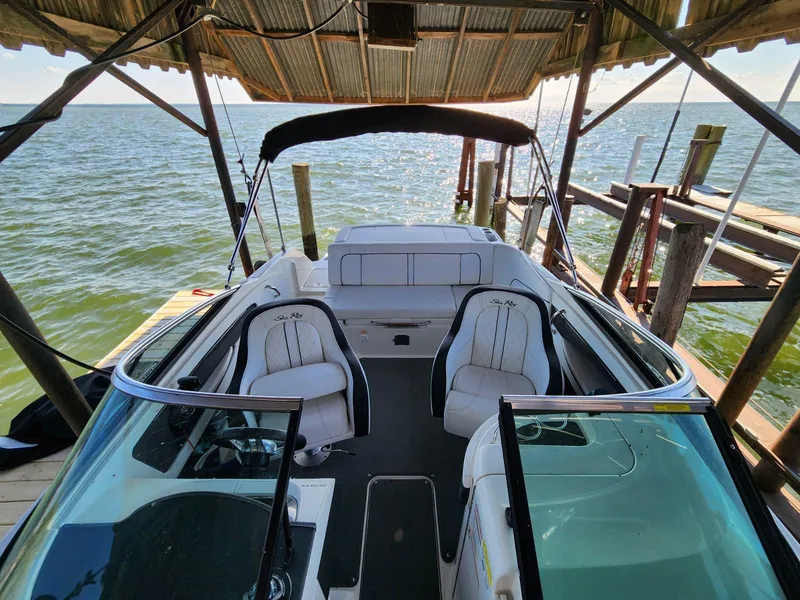 Slide: The Image of The image shows a 2015 Sea Ray 220 Sundeck boat docked. It features white seats and a black canopy. - 23