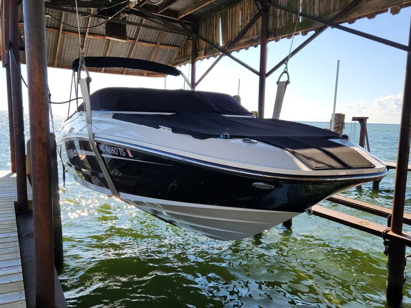 The Image of A 2015 Sea Ray 220 Sundeck is suspended on a boat lift over the water. It has a black cover. - 0