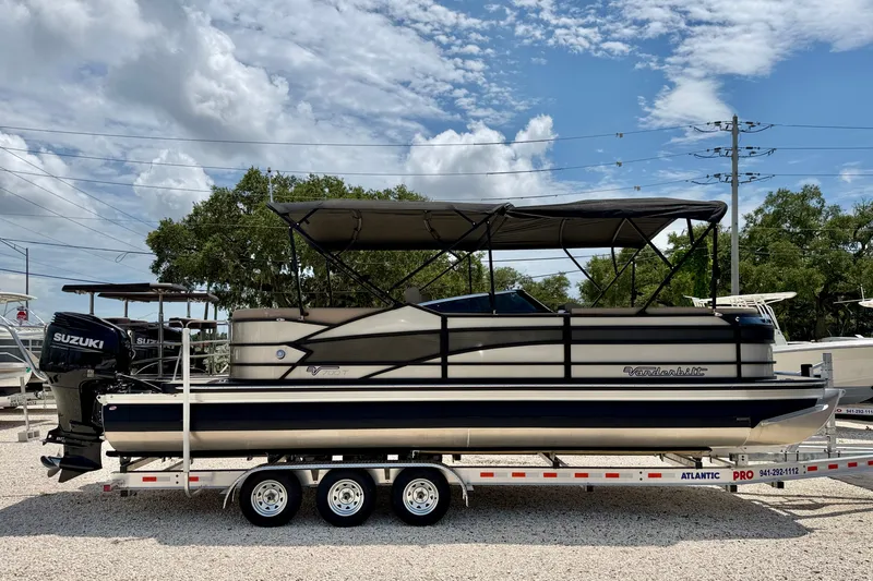 The Image of 2027 Vanderbilt 700T pontoon boat on trailer, featuring Suzuki outboard motor, under a cloudy sky. - 0
