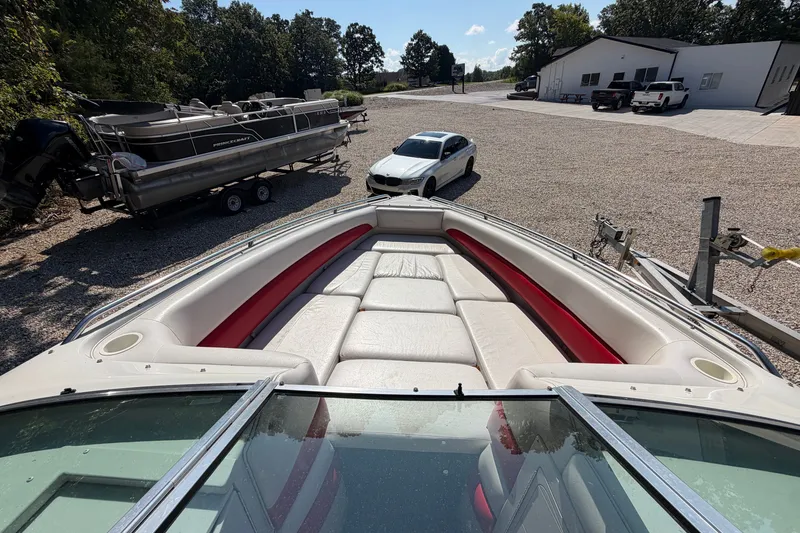 Slide: The Image of 2006 Crownline 266 BR boat with red and white seating, parked near vehicles and trees. - 11