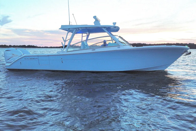 Slide: The Image of 2023 Cobia 330 Dual Console boat on water at sunset. - 2