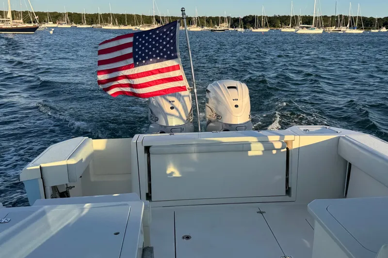 Slide: The Image of 2023 Cobia 330 Dual Console boat with American flag, twin engines, on a scenic waterway. - 19