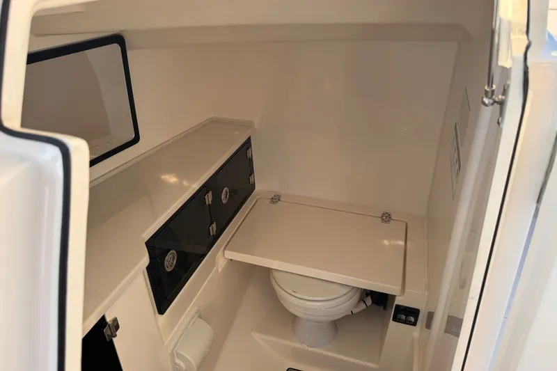 Slide: The Image of 2023 Cobia 330 Dual Console boat interior with compact marine toilet and storage. - 16