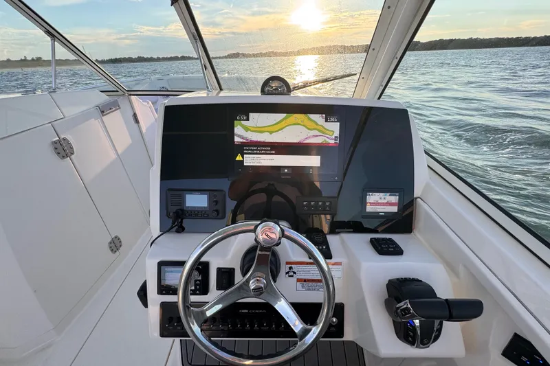Slide: The Image of 2023 Cobia 330 Dual Console helm with navigation display, steering wheel, and throttle controls at sunset. - 10