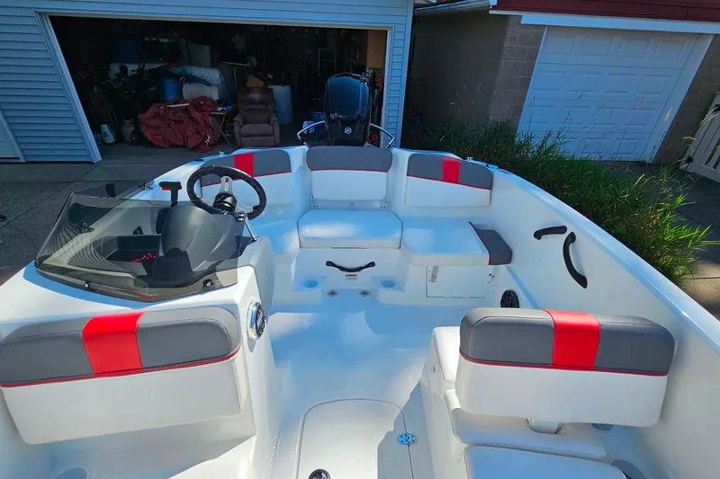 Slide: The Image of 2022 Tahoe T16 boat interior with red and gray seating, parked near a garage. - 8