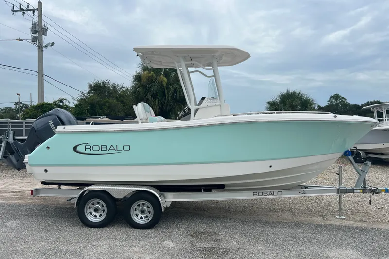 The Image of 2025 Robalo R230 Center Console boat on trailer, light blue hull, parked outdoors. - 1