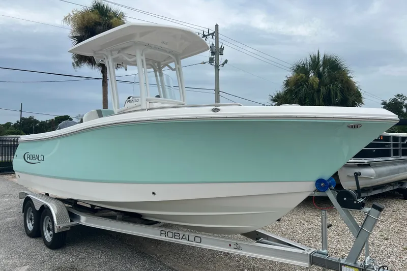 Slide: The Image of 2025 Robalo R230 Center Console boat on trailer, light blue hull, parked outdoors. - 2