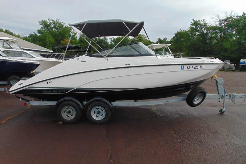 Slide: The Image of 2018 Yamaha Boats SX210 on trailer, parked outdoors with other boats nearby. - 2