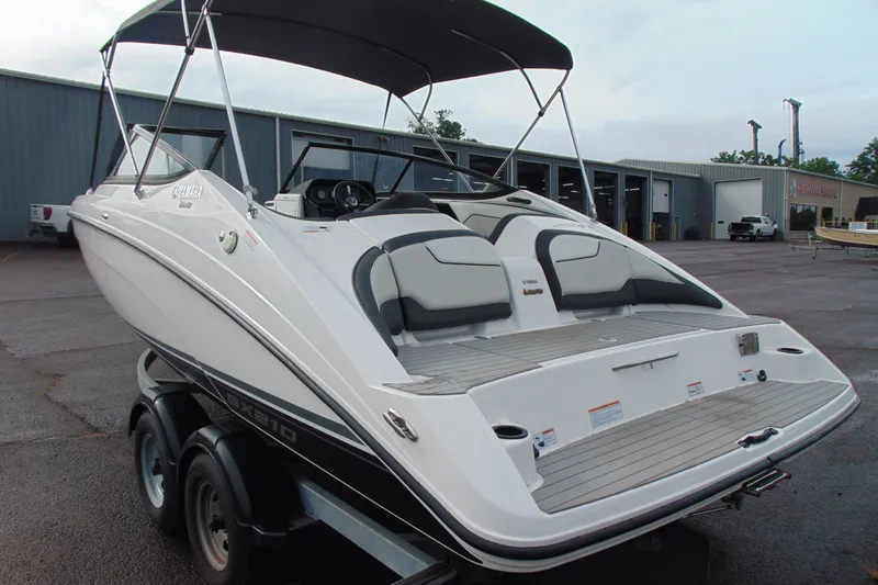 Slide: The Image of 2018 Yamaha Boats SX210 on trailer, parked outdoors near industrial buildings. - 5