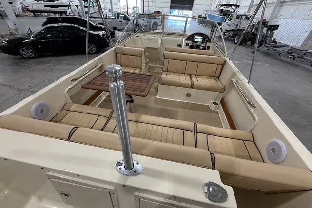 Slide: The Image of 2023 Rossiter 23 boat interior with beige seating and wooden table in a spacious garage. - 7