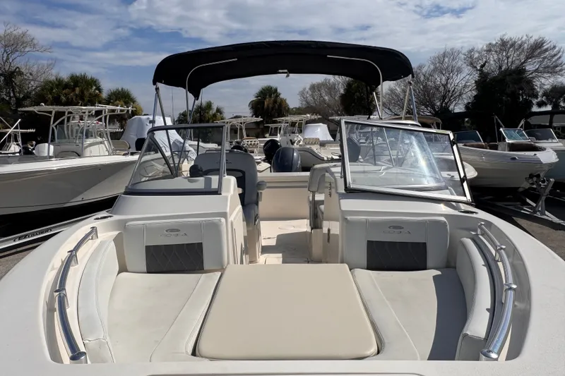 Slide: The Image of 2023 Cobia 220 Dual Console boat with seating, windshield, and canopy in a marina setting. - 15