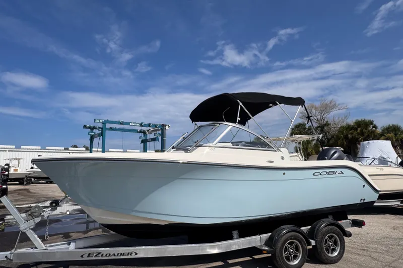 The Image of 2023 Cobia 220 Dual Console boat on trailer under clear blue sky. - 1