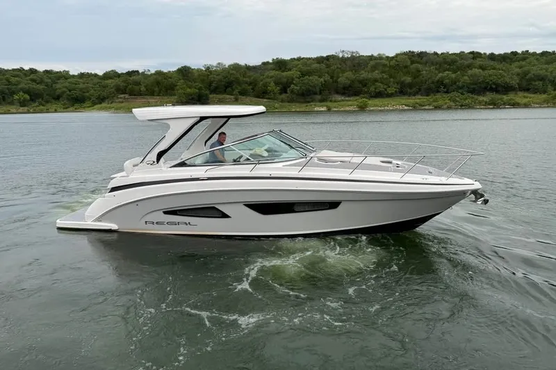 Slide: The Image of 2025 Regal 33 Express boat cruising on a serene lake with lush green shoreline. - 1