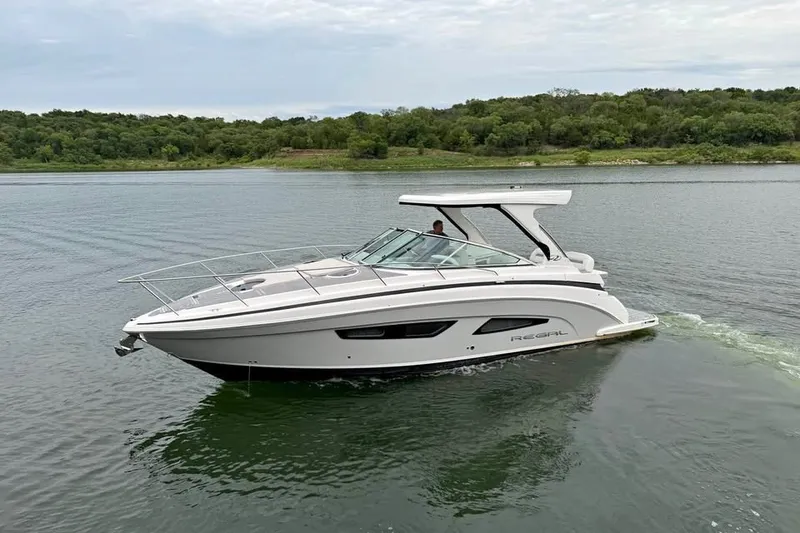 The Image of 2025 Regal 33 Express boat cruising on a serene lake with lush green shoreline. - 0