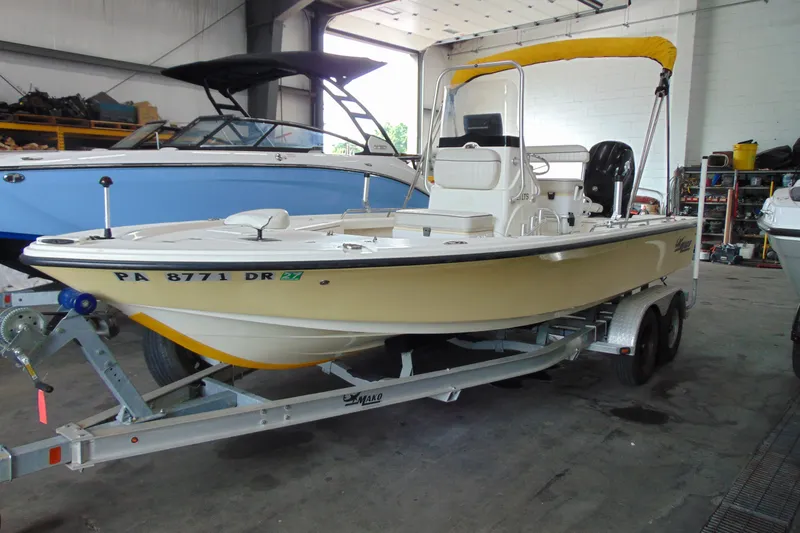 The Image of 2015 Mako 21 LTS boat on trailer in a garage, featuring a yellow hull and white interior. - 1