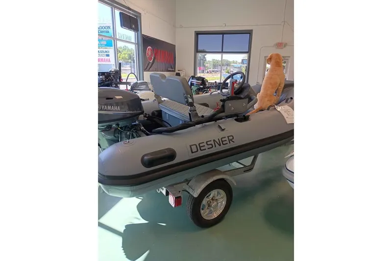 Slide: The Image of A dog sits on a 2026 DESNER ALUMINUM CL 310 inflatable boat in a showroom. - 2