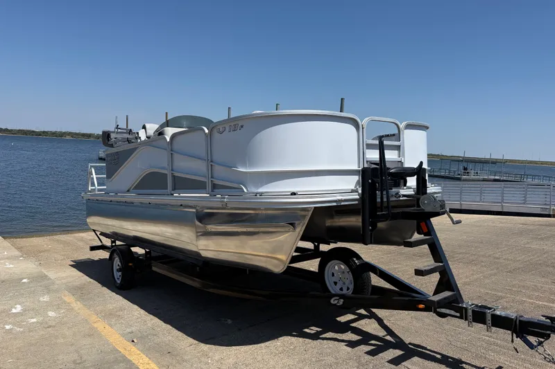 The Image of 2020 SunCatcher V18 Fish boat on trailer by a lake under clear blue sky. - 0