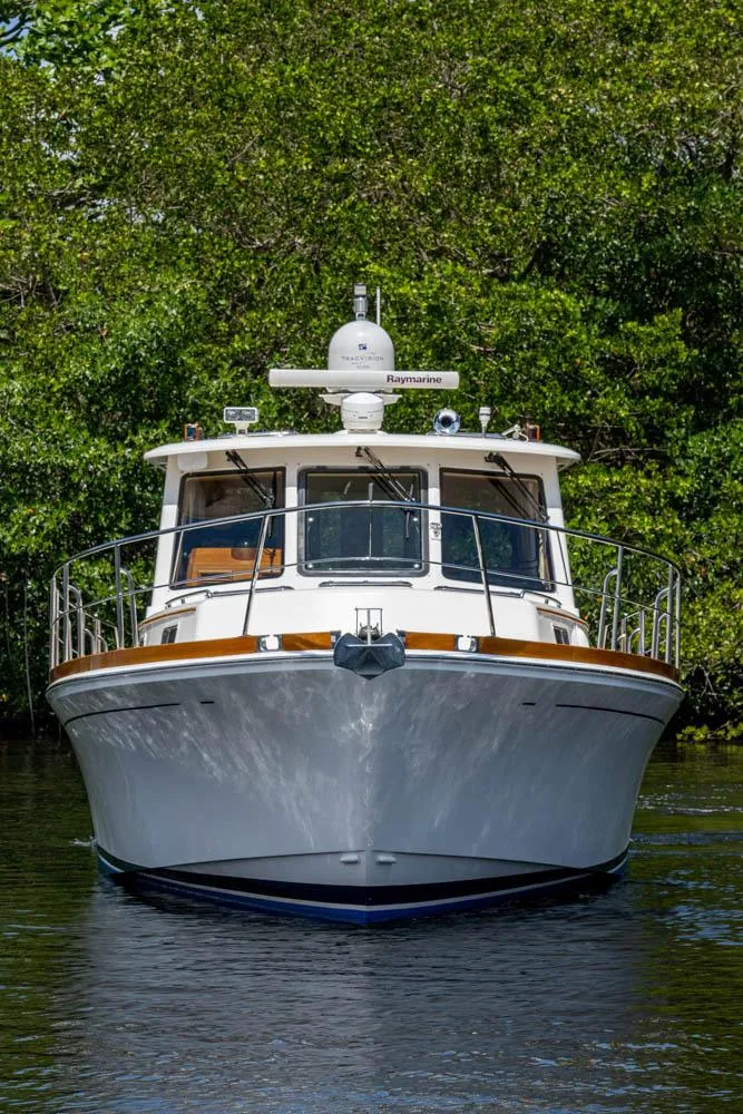 Slide: The Image of 2007 Grand Banks 43 Eastbay SX with a white hull and wood accents, set against lush greenery. - 9