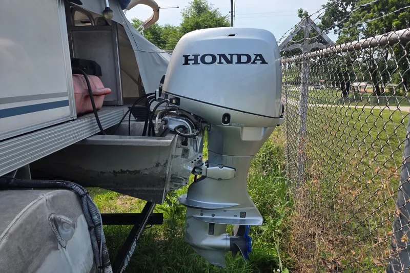Slide: The Image of 2007 Quest mini pontoon with Honda outboard motor near chain-link fence. - 7