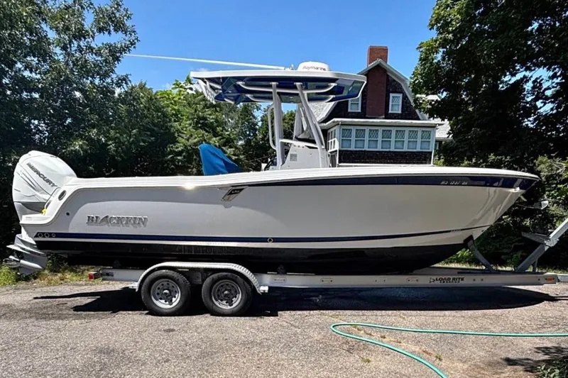 Slide: The Image of 2019 Blackfin 242 CC boat on trailer, parked outdoors near a house. - 0