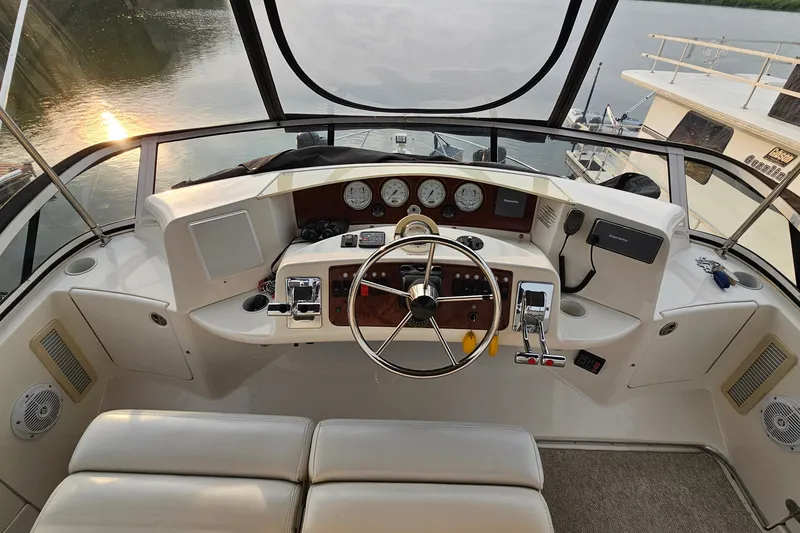 Slide: The Image of 2003 Silverton 35 Motor Yacht helm with steering wheel, gauges, and controls, overlooking serene water. - 14