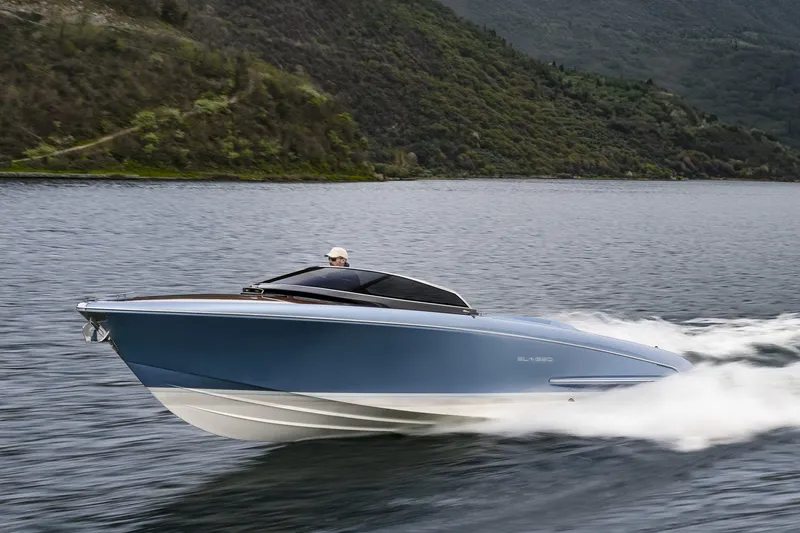 Slide: The Image of 2004 Riva El-Iseo speedboat cruising on a scenic lake with lush green hills. - 1