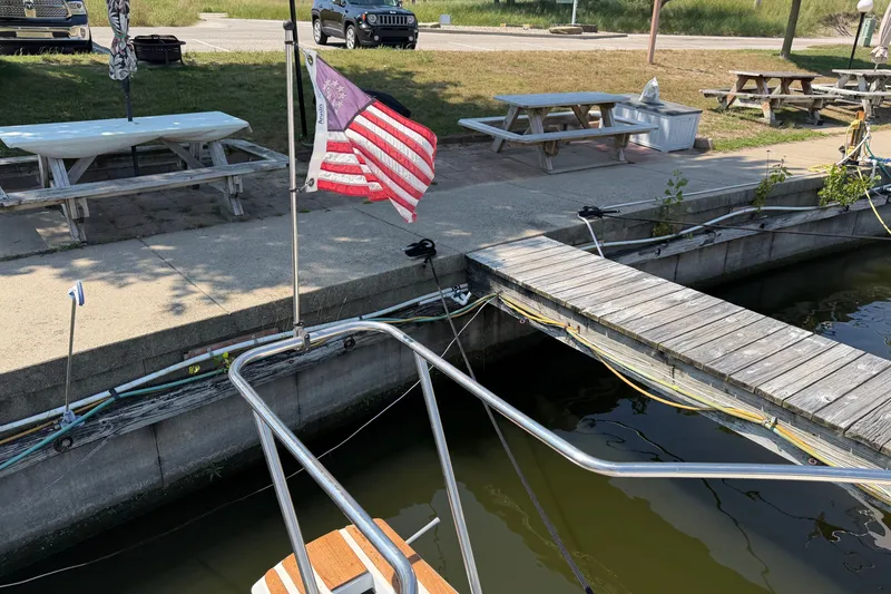 Slide: The Image of Docked 1987 Silverton 34 Convertible with American flag, near picnic tables and parked vehicles. - 37