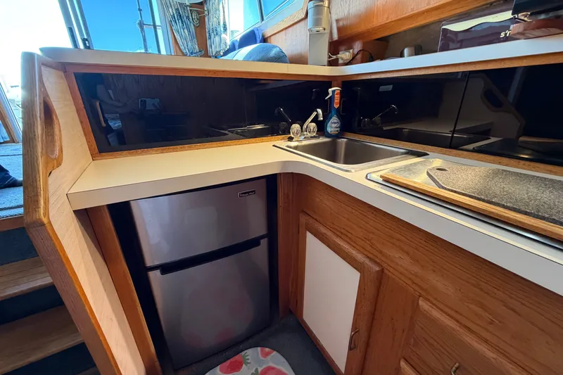 Slide: The Image of 1987 Silverton 34 Convertible yacht kitchen with sink, mini fridge, and wooden cabinetry. - 26