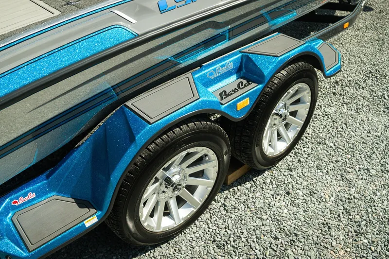 Slide: The Image of 2026 Bass Cat Lynx STS trailer with blue metallic finish and dual wheels on gravel. - 24