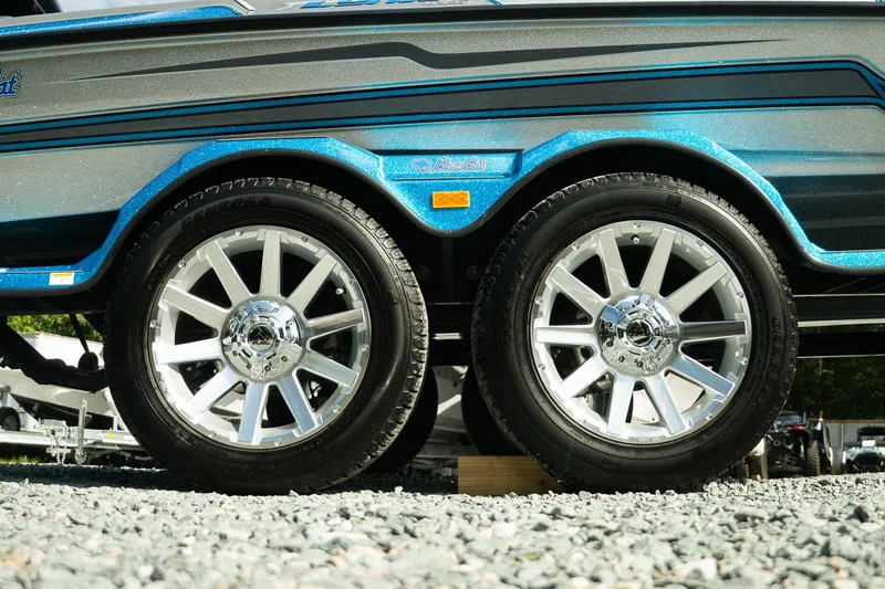 Slide: The Image of 2026 Bass Cat Lynx STS trailer with shiny chrome wheels on gravel surface. - 23