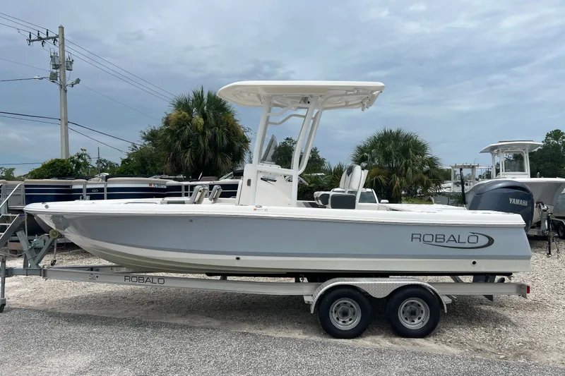 The Image of 2024 Robalo 226 Cayman boat on trailer, parked outdoors under cloudy sky. - 1