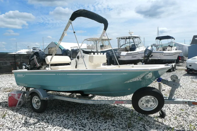 Slide: The Image of 2027 Boston Whaler 150 Montauk boat on trailer, parked in a marina under a cloudy sky. - 3